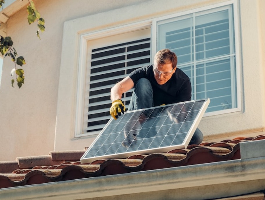 Man in gloves holding a solar panel on the roof